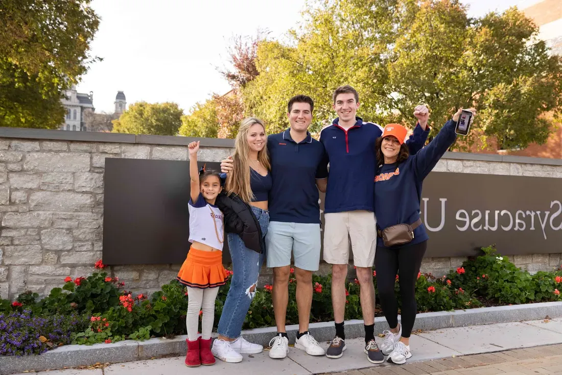 A family stands together in front of the Syracuse University sign during family weekend.